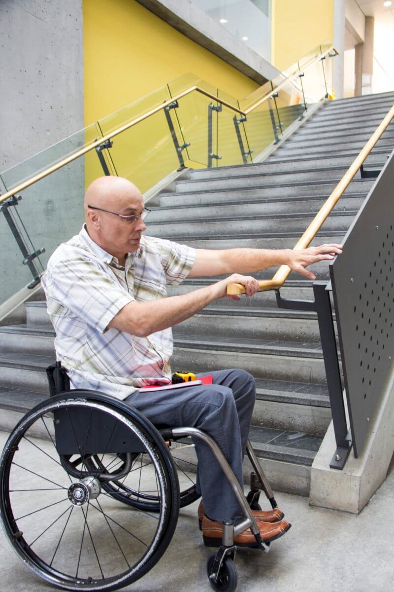 A man in a wheelchair assesses a staircase handrail.