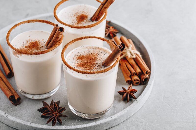 Homemade vanilla drink Eggnog in glass with grated nutmeg and cinnamon sticks