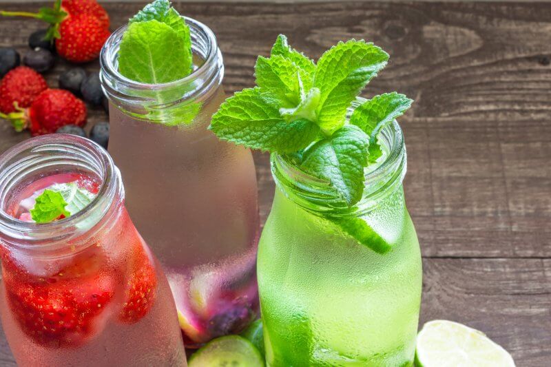 Variety of cold drinks in small bottles with fruits, berries, cucumber and mint.