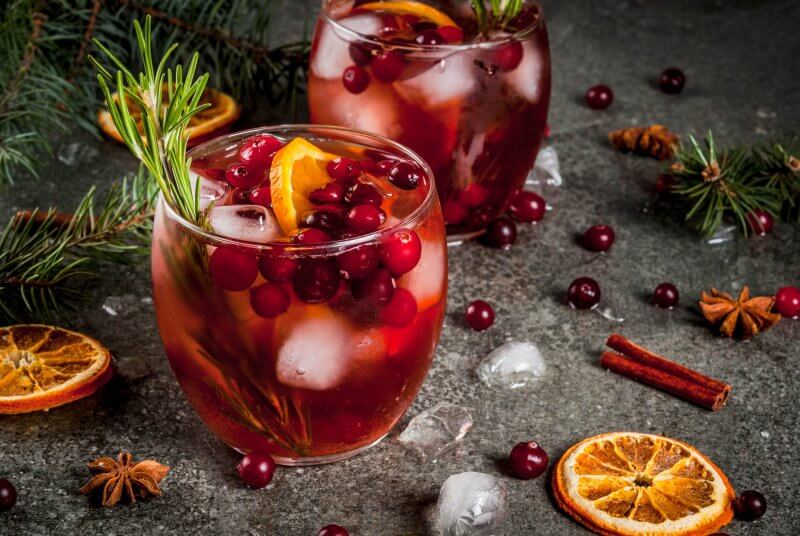 Mocktail with cranberries, orange, rosemary, with spices (cinnamon, anise) and ice, on a dark stone table
