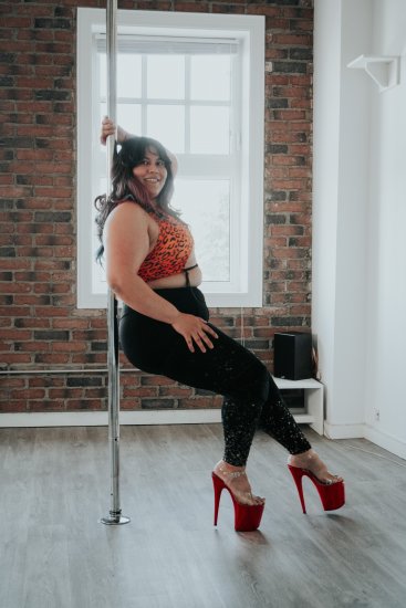 Aileen leaning against a pole at her Edmonton pole dancing studio