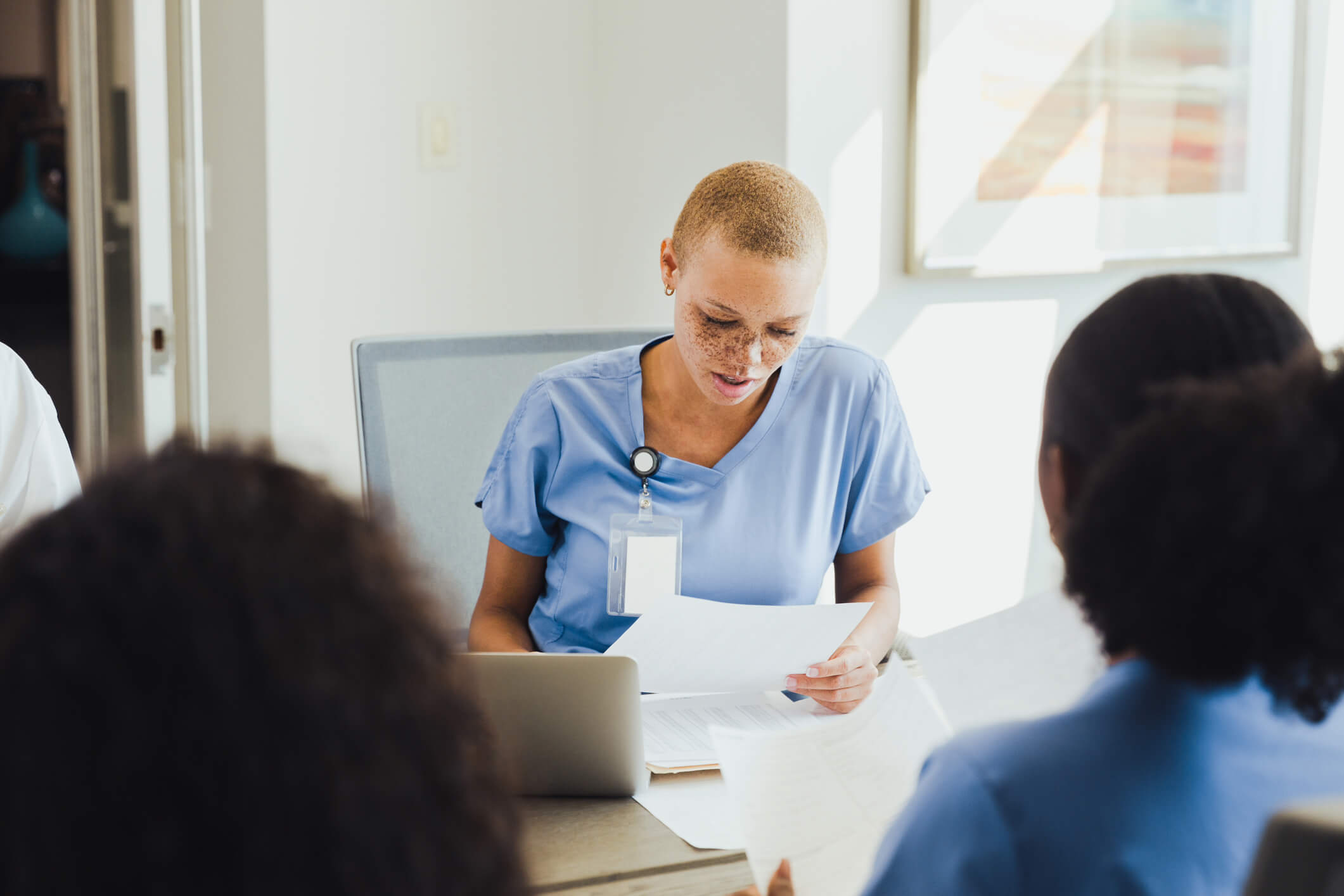 A healthcare professional reads a medical document during a meeting with a group of colleagues.