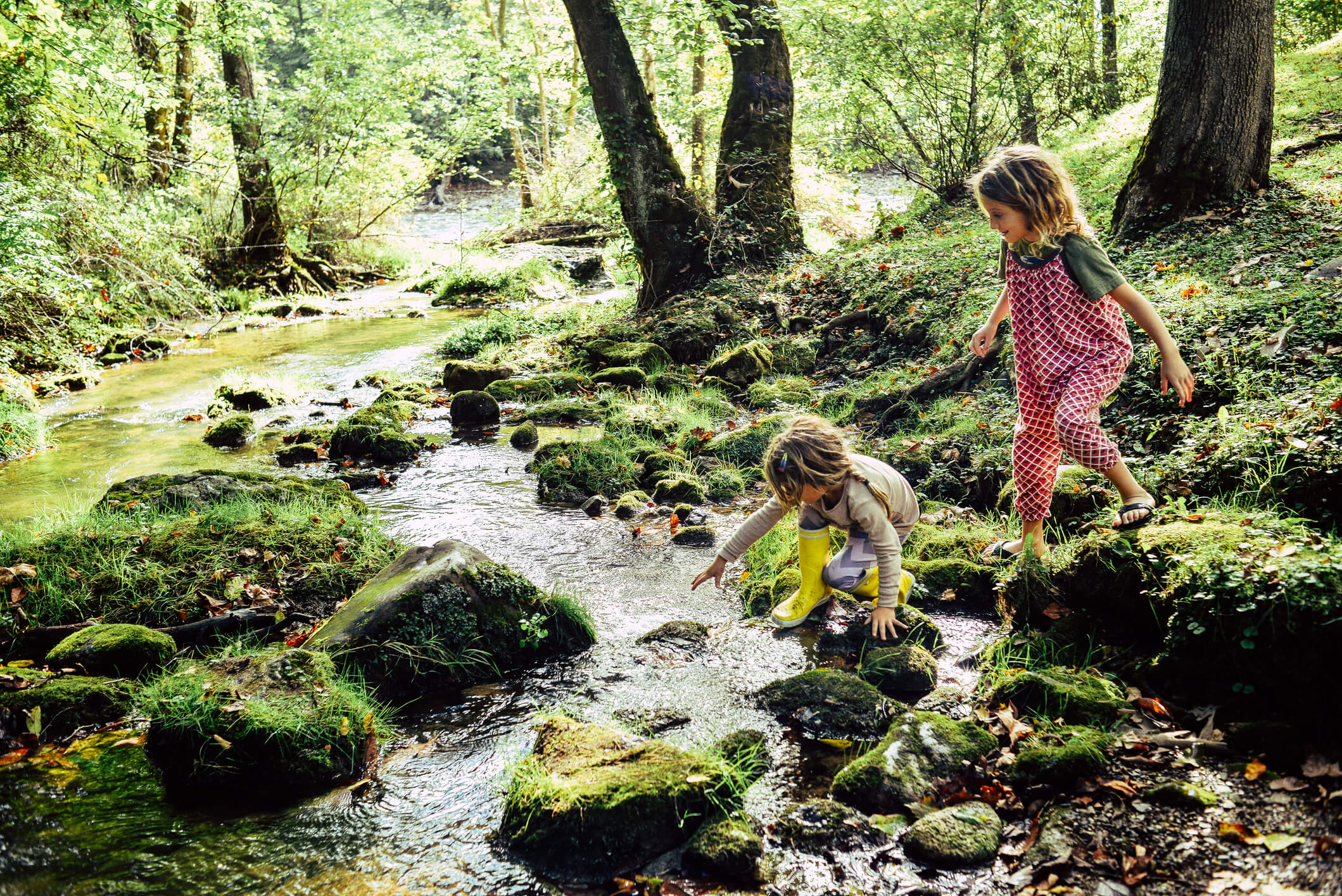 Two children having an adventure, climbing and stepping in a river exploring a beautiful natural area.