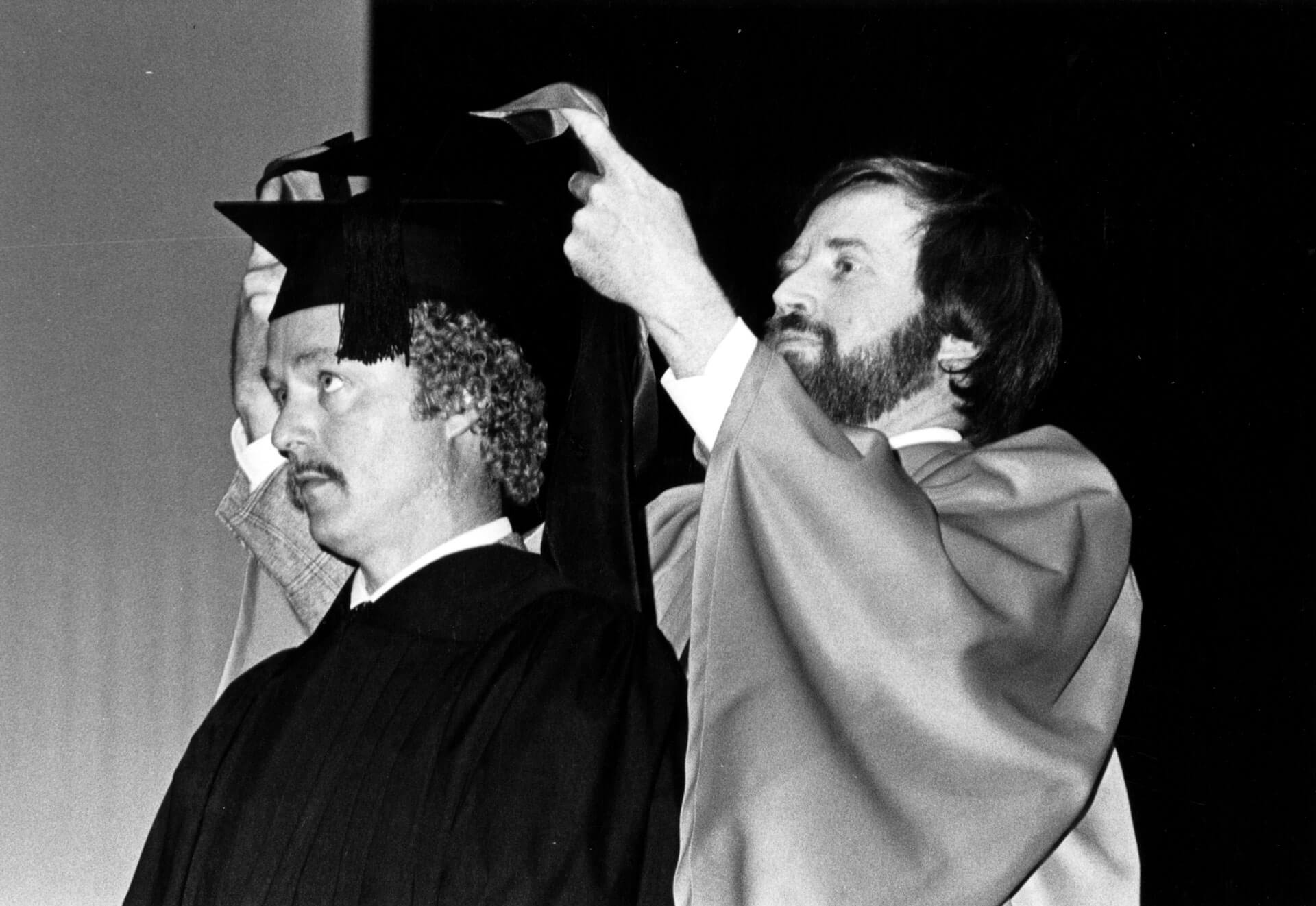 Neil Henry places a convocation hood on the shoulders of a university graduate circa 1980.
