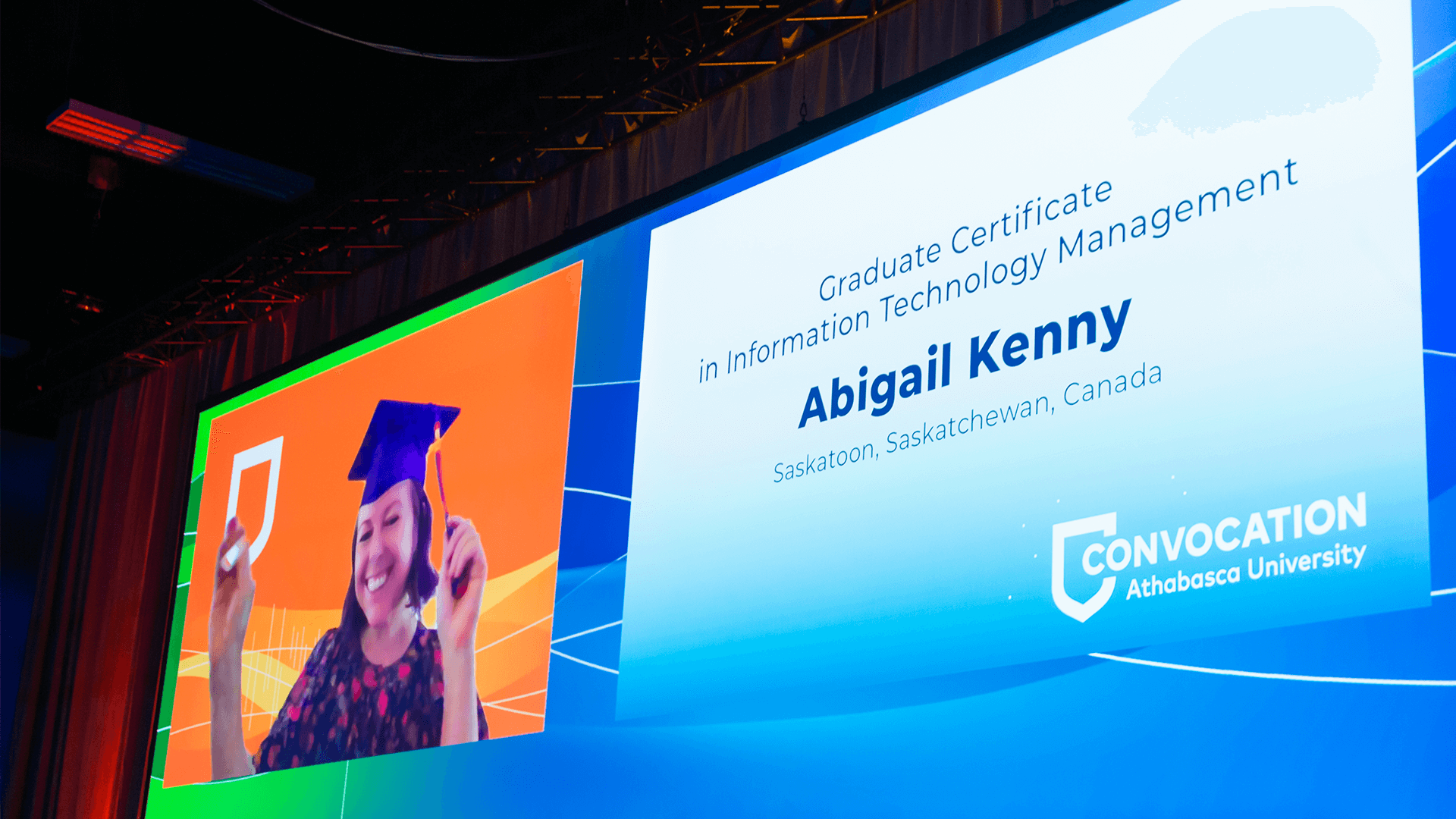 Shot of the big screen in the convocation ceremony showing a virtual graduate attendee and her name and program