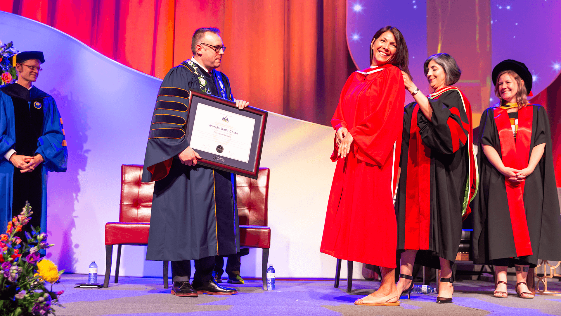 Dr. Alex Clark holding an honoary degree for Wanda Dalla Costa who is receiving her hood from faculty of humanities and social sciences dean Dr. Manijeh Mannani